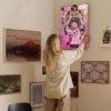 Woman hanging Lionel Messi GOAT poster on gallery wall in modern home interior with mixed art collection