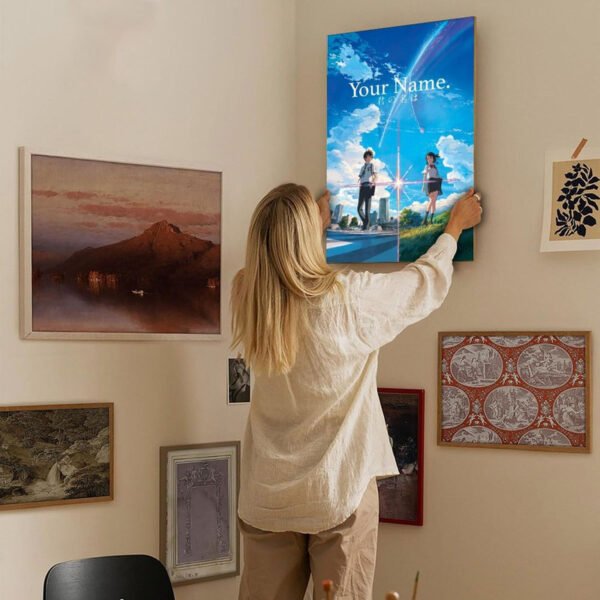 Woman hanging Your Name anime canvas poster on gallery wall in modern home with eclectic art collection, showcasing anime home decor integration.