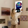 Woman hanging animated movie canvas print on gallery wall in modern home interior with multiple framed artworks.