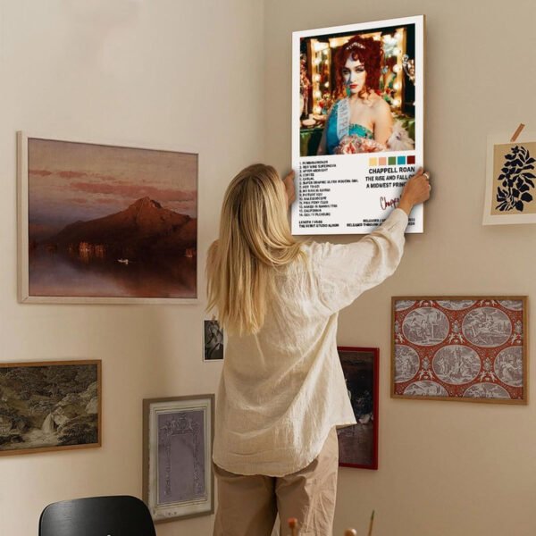 Person hanging Chappell Roan "Midwest Princess" album poster on eclectic gallery wall featuring vintage maps, landscape paintings, and contemporary art in modern home interior