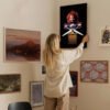 Woman hanging Chucky horror doll artwork on gallery wall surrounded by eclectic art collection in modern home interior
