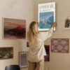 Woman hanging Coastal Life canvas print on gallery wall showcasing coastal home decor and interior design styling