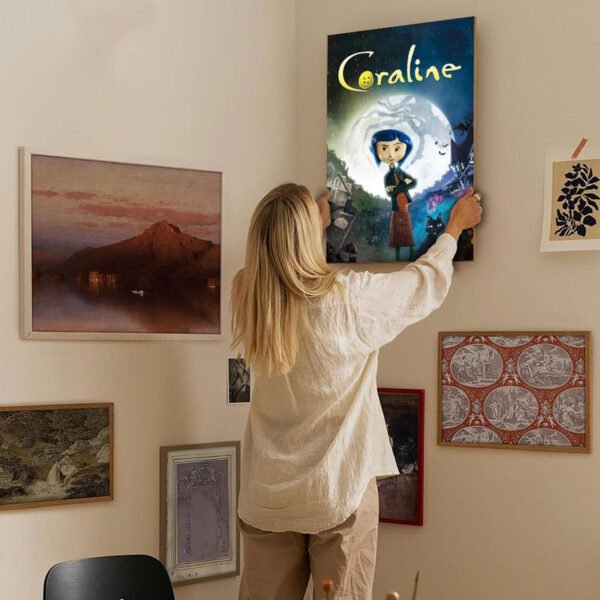 Person hanging Coraline movie poster on curated gallery wall with mixed framed artworks in modern home interior.