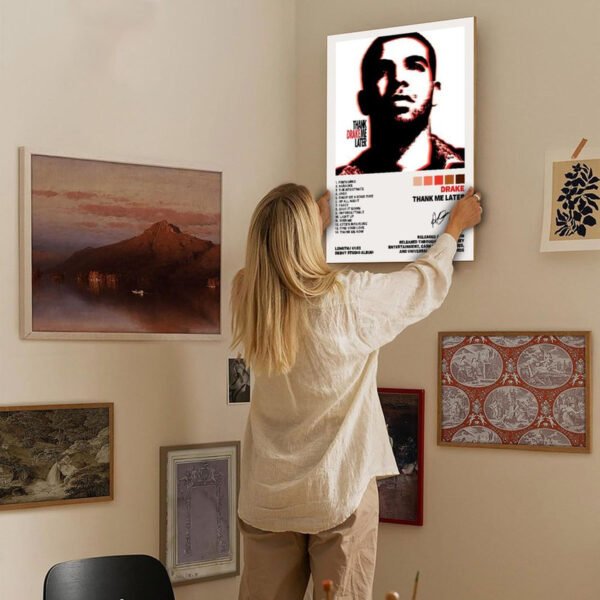 Woman hanging Drake Thank Me Later poster on eclectic gallery wall with landscape art, vintage maps, and botanical prints in cozy home interior