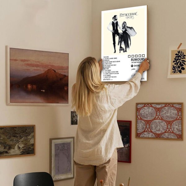 Person hanging Fleetwood Mac Rumours album poster on gallery wall with eclectic art collection including landscape paintings and vintage maps, demonstrating music memorabilia integration in home interior design and wall decor styling inspiration.
