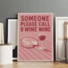 Framed wine-themed poster print "Someone Please Call 9 Wine Wine" with pink background, wine glass and cheese illustration, displayed in professional studio setting.