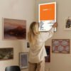 Person hanging Frank Ocean Channel Orange poster on eclectic gallery wall with mixed art collection