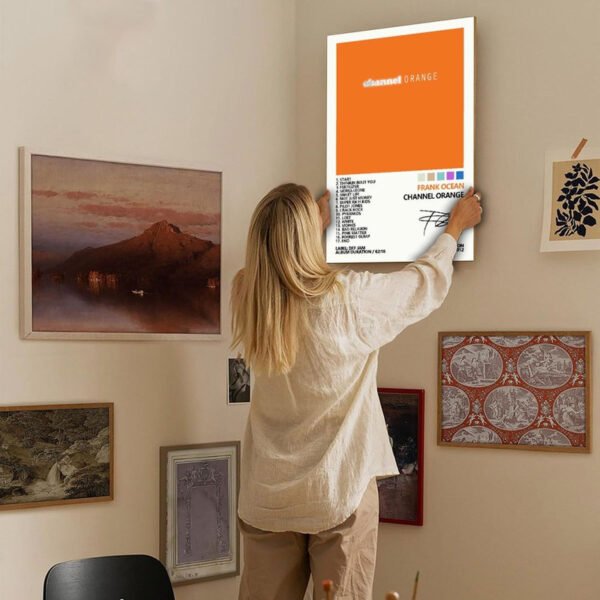 Person hanging Frank Ocean Channel Orange poster on eclectic gallery wall with mixed art collection