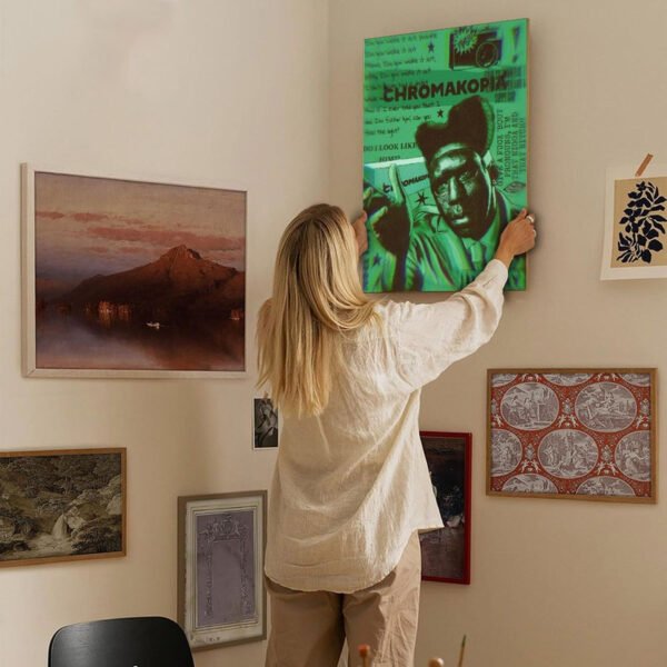 Person hanging contemporary green art poster on curated gallery wall featuring diverse framed artworks in modern interior design setting