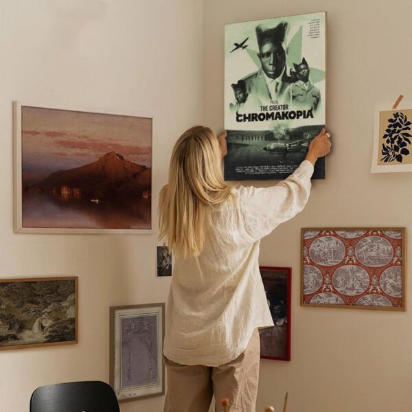 Woman hanging CHROMAKOPIA poster on gallery wall with multiple framed artworks in cozy home interior design setting