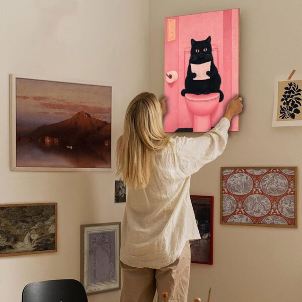 Woman hanging funny cat bathroom art print on eclectic gallery wall in modern home interior.