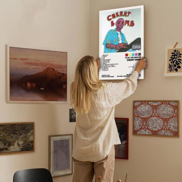 Young woman hanging Tyler The Creator Cherry Bomb poster on eclectic gallery wall with vintage art and photography