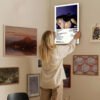 Person hanging Olivia Rodrigo GUTS poster on curated gallery wall featuring eclectic mix of art prints, vintage maps, and contemporary decor in bohemian-style living space