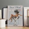 Unframed "Guest Check" disco ball martini art print displayed in minimalist Scandinavian-style interior with neutral decor and empty picture frames on hardwood floor.