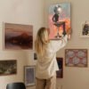 Woman hanging contemporary disco ball art in curated gallery wall display at home.