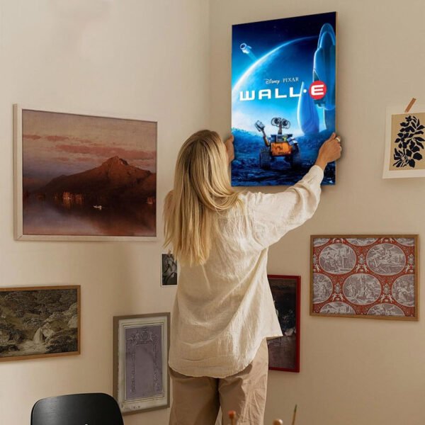 Person hanging Disney Pixar WALL-E movie poster on gallery wall as part of home decor arrangement.