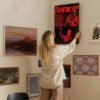 Person hanging Friday the 13th horror movie poster on gallery wall with eclectic art collection in modern home interior