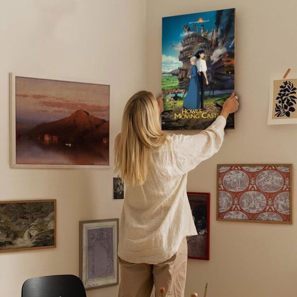 Person arranging Howl's Moving Castle poster on eclectic gallery wall featuring various framed artworks in modern home interior.