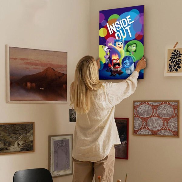 Woman hanging Inside Out movie poster on gallery wall with eclectic art collection in modern home interior design.