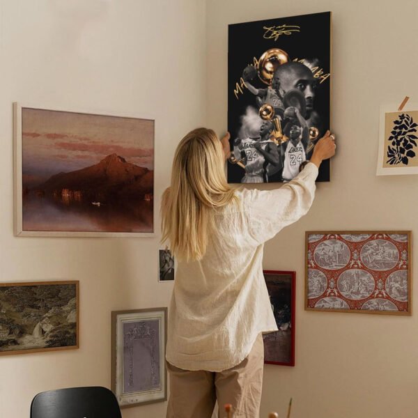 Woman hanging Kobe Bryant memorial canvas on gallery wall in home interior with diverse art collection and contemporary decor styling