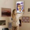 Woman hanging LeBron James Lakers poster on gallery wall with mixed art collection in modern home interior
