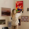 Woman hanging Lion King canvas poster on gallery wall with mixed artwork creating stylish Disney home decor display in modern living space.