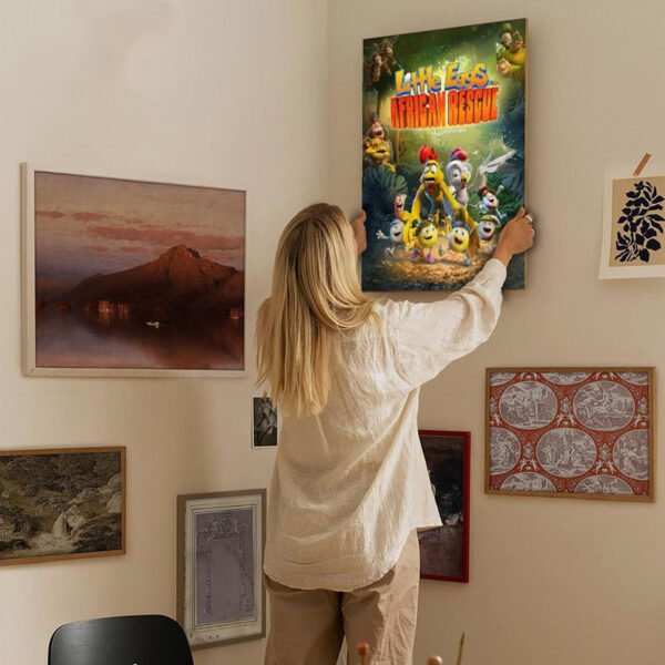 Woman hanging Little Eggs African Rescue movie poster on gallery wall in modern home interior with various framed artwork for stylish family-friendly wall decor.
