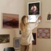 Woman hanging Melanie Martinez Portals album poster on gallery wall with eclectic art collection in modern home interior