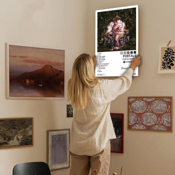 Woman hanging Melanie Martinez Portals album poster on gallery wall with eclectic art collection in modern home interior