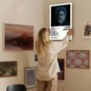 Person hanging The Weeknd Dawn FM poster on gallery wall with framed art in modern home interior