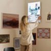 Woman hanging Radiohead OK Computer poster on gallery wall with eclectic art collection in modern home interior