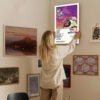 Woman hanging Kanye West Graduation album poster on gallery wall with mixed artwork for home decor inspiration