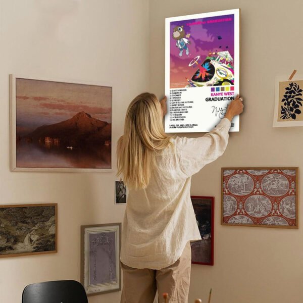 Woman hanging Kanye West Graduation album poster on gallery wall with mixed artwork for home decor inspiration