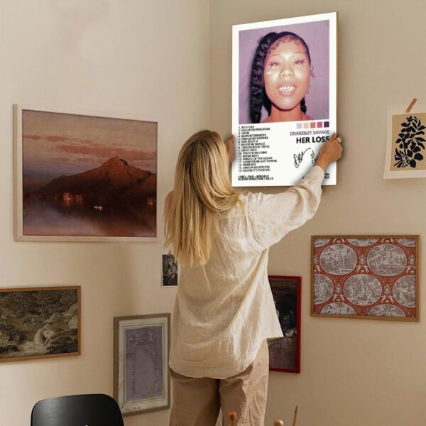 Person hanging Drake 21 Savage Her Loss album poster on curated gallery wall in contemporary home interior