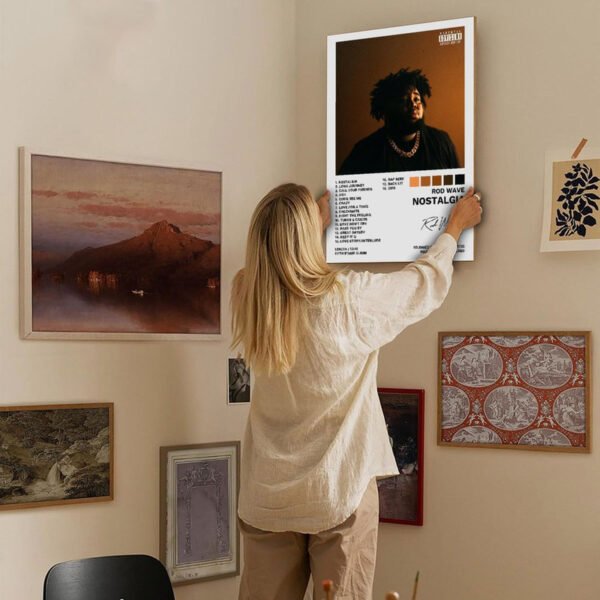 Person hanging Rod Wave Nostalgia album canvas print on gallery wall with other framed artworks in modern home interior.