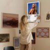 Person hanging Sabrina Carpenter Short n Sweet album poster on gallery wall with various artworks