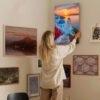 Woman hanging Santorini sunset canvas art in modern gallery wall home decor setting