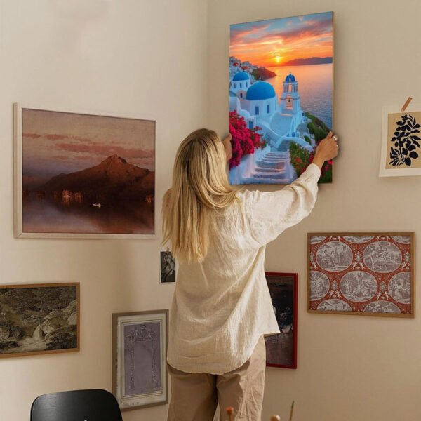 Woman hanging Santorini sunset canvas art in modern gallery wall home decor setting