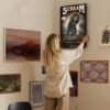 Person hanging vintage Scream movie poster on gallery wall with eclectic art collection for home decor inspiration
