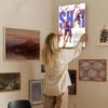 Woman hanging SGA Thunder basketball poster on curated gallery wall with mixed art collection in modern home interior