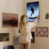 Woman hanging Spider-Man Into the Spider-Verse poster on gallery wall showing home decor styling with movie art integration.