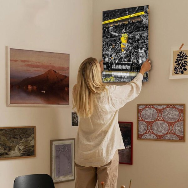 Woman hanging LeBron James Lakers canvas print on curated gallery wall showcasing sports art integration in modern home decor