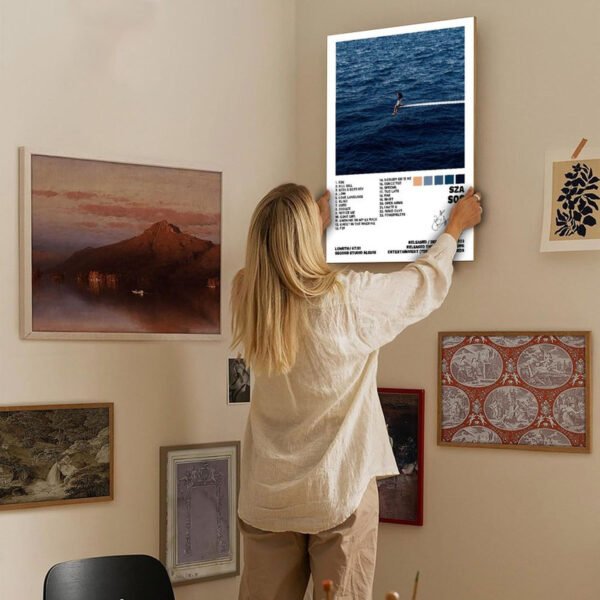 Person hanging SZA SOS album poster on gallery wall showcasing music artwork as contemporary home decor