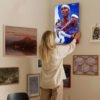 Woman hanging Thunder basketball artwork on curated gallery wall featuring mixed art collection in modern home
