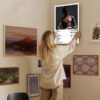 Woman hanging Travis Scott Rodeo album poster on gallery wall as home decor art in modern interior design setting