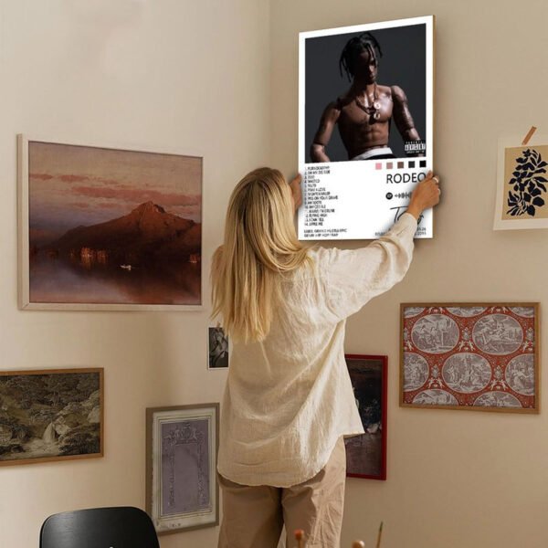 Woman hanging Travis Scott Rodeo album poster on gallery wall as home decor art in modern interior design setting