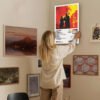 Person hanging Twenty One Pilots Clancy album poster on gallery wall with various framed artworks in home interior