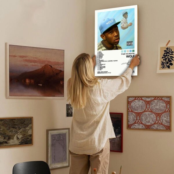 Person hanging Tyler The Creator WOLF album poster on curated gallery wall with eclectic art collection in modern home interior