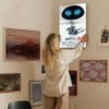 Person hanging WALL-E Disney Pixar movie poster on gallery wall with various framed artworks in home interior.
