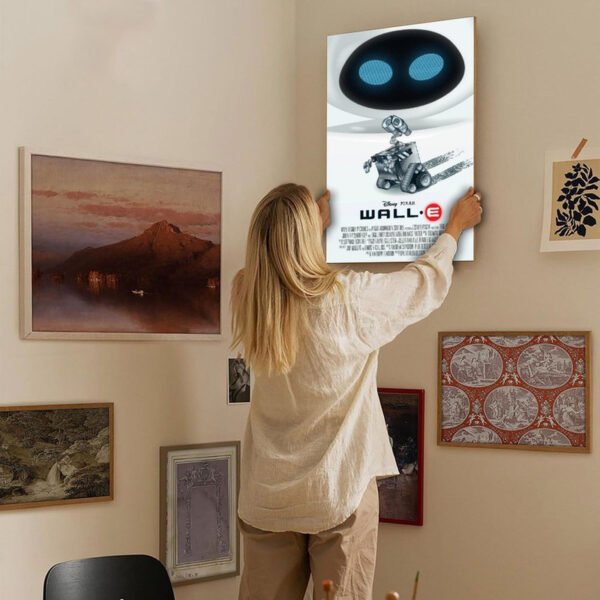 Person hanging WALL-E Disney Pixar movie poster on gallery wall with various framed artworks in home interior.